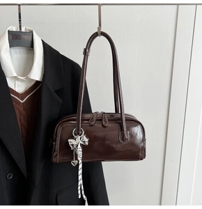 Détail d'un sac Boston en cuir brillant marron foncé avec breloque nœud argenté