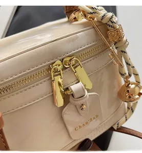 Gros plan détaillé des fermetures éclair dorées et breloques d'un sac boîte beige