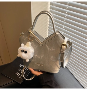 Détail du sac à main gris en cuir avec ouverture en V et breloque en peluche douce