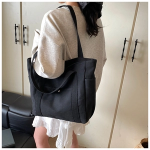 Model trägt eine große schwarze Segeltuchtasche mit Doppelgriffen in einer gemütlichen Wohnung