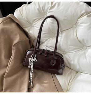 Détail du sac Boston en cuir brillant marron foncé avec pendentif nœud argenté et fermetures