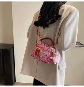 Detail of pink tweed handbag with red handle and plush monster charm on shoulder