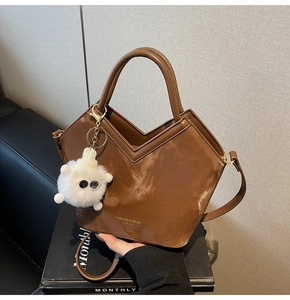 Détail d'un sac seau en cuir marron avec bord en V et breloque pompon en peluche blanche