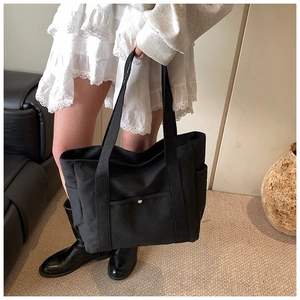 Detail of black canvas tote bag showing side pockets and long shoulder straps