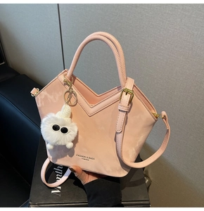 Détail du sac en cuir verni rose avec ouverture en V et breloque en peluche blanche