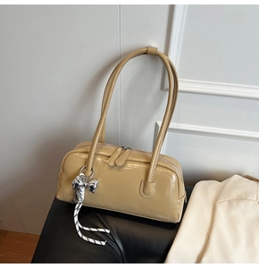Détail du sac Boston en cuir verni beige avec finition brillante et breloque nœud