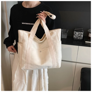 Detail of a large off-white canvas tote bag showing side pockets and versatile straps