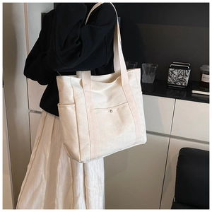 Detail of minimalist cream canvas tote bag with front snap pocket and side compartment