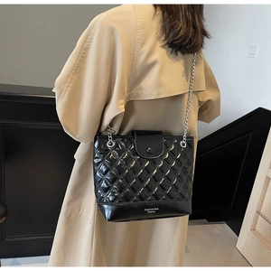 Detail of black quilted leather bucket bag with silver chain strap on trench coat