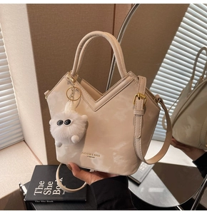 Détail d'un sac seau crème texturé avec bandoulière et pendentif monstre en peluche