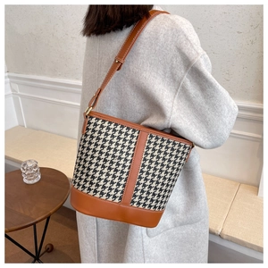 Detail view of houndstooth bucket bag with brown leather strap worn over a wool coat