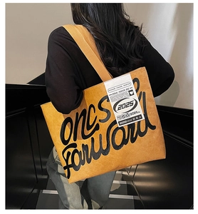 Détail d'un grand sac cabas jaune avec typographie noire porté par un mannequin