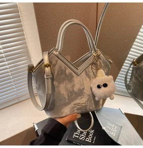 Détail du sac seau argenté mat avec une breloque monstre en peluche et bandoulière