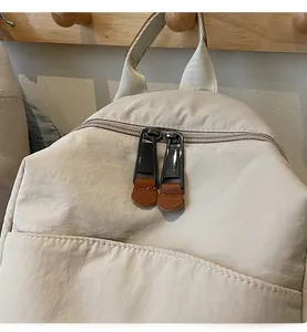 Detail of smooth double zipper with brown leather pulls on beige nylon backpack