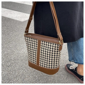 Détail du sac seau en motif pied-de-poule avec bordure en cuir et bandoulière réglable