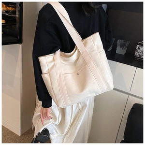 Spacious beige canvas tote bag with side pockets and sturdy straps shown on model