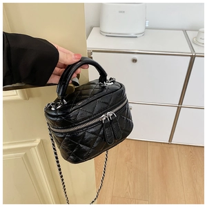 Détail d'un mini sac seau matelassé noir avec bandoulière chaîne porté à la main