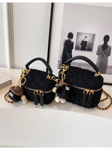 Black tweed crossbody bag with gold chain and plush keychain in a minimalist studio setting