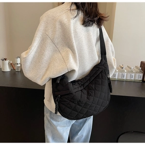 Detail of black quilted half-moon crossbody bag with adjustable wide strap on model