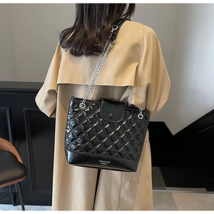 Close-up of black quilted bucket bag with silver chain strap on trench coat