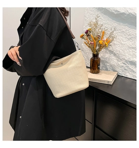 Détail du sac seau crème avec texture tissée, bandoulière en cuir marron et boucle