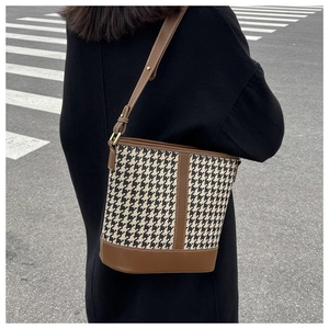 Detailed close-up of stitching on brown leather and houndstooth fabric bucket bag