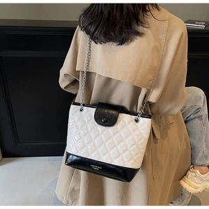 Close-up of quilted black and white chain bucket bag on a model wearing a beige coat
