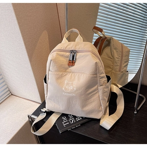 Close-up of beige nylon backpack with white cat embroidery and dual metal zippers