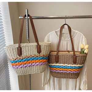 Detail of woven straw tote bags featuring colorful rainbow straps and brown leather handles