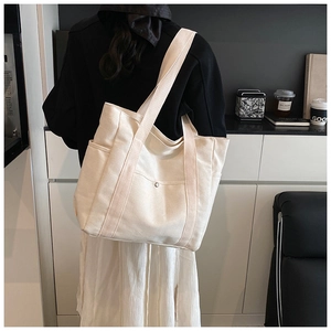 Detail of a cream canvas tote bag showing side pockets and metal buckle for daily use