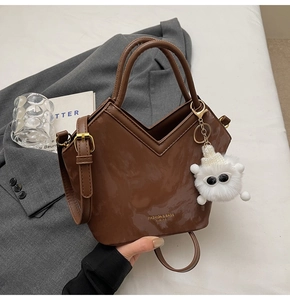 Détail du sac seau en cuir verni marron foncé avec coupe en V et breloque monstre en peluche