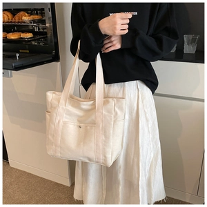 Close-up of cream canvas tote bag with side pockets and metal snap button detail
