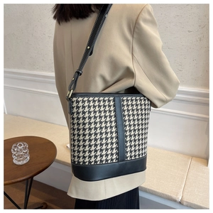 Détail du sac seau pied-de-poule avec bandoulière en cuir et coutures sur bois