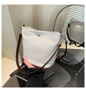Gros plan du sac seau tissé crème avec bouton pression argenté et sangle en cuir brun