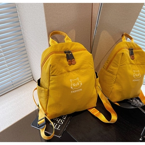 Detail view of yellow nylon backpack featuring cat print and side pockets via mirror reflection