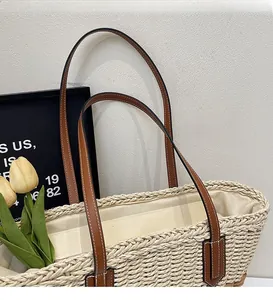 Detail of straw tote bag showing smooth brown leather shoulder strap with white stitching