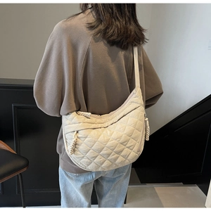 Detail of beige quilted crescent bag featuring wide shoulder strap and woven zipper pull