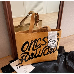 Détail du sac cabas marron avec lettrage artistique noir et étiquette latérale décontractée