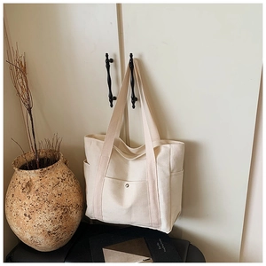 Detail of off-white canvas tote bag featuring metal buckle pocket and side storage