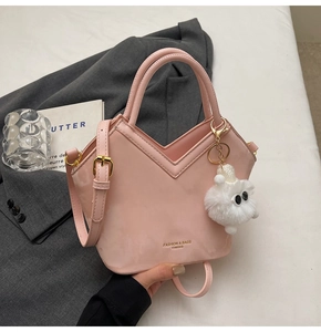 Gros plan du sac seau en cuir verni rose avec ouverture en V et breloque en peluche
