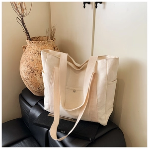 Detailed close-up of a beige canvas tote bag with side pockets and metal snap button