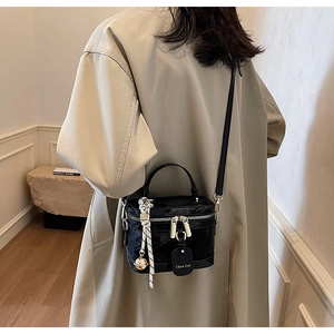 Vue latérale du sac boîte noir en cuir verni brillant avec bandoulière et pendentif cloche
