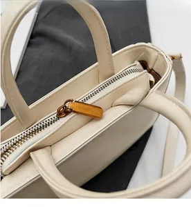 Macro shot of smooth gold-tone zipper on creamy beige faux leather crossbody handbag