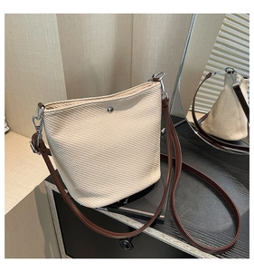 Détail du sac seau en paille tressée beige avec bandoulière en cuir brun et fermoir