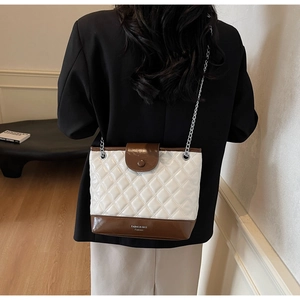 Detail of white quilted tote with brown leather base and silver chain strap on model