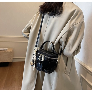 Détail d'un sac cylindrique noir avec foulard en soie porté sur un trench beige