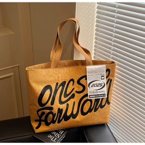 Gros plan du sac cabas jaune gingembre avec lettrage noir et texture de tissu plissé