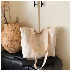 Close-up of cream canvas tote bag with metal snap pocket and sturdy shoulder straps