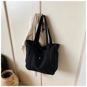 Detail of a black canvas tote bag with front metal button pocket hanging in a room