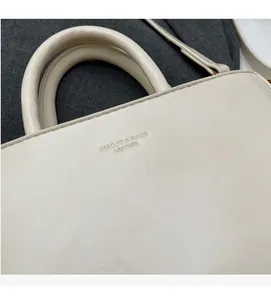 Detail shot of the embossed brand logo on the off-white leather surface of the handbag